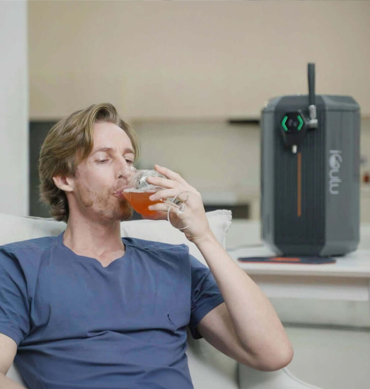 Man enjoying a drink with the iGulu S1 Cyber Week Starter Home Brewer Smart Bundle in the background.